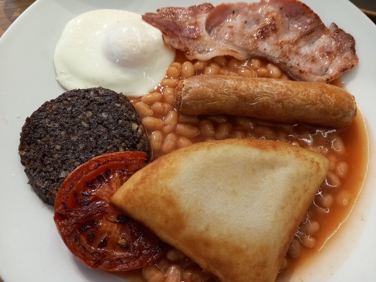A Scottish breakfast: a fried egg, bacon, a link sausage, black pudding, a grilled tomato, a triangle of potato scone and baked beans.