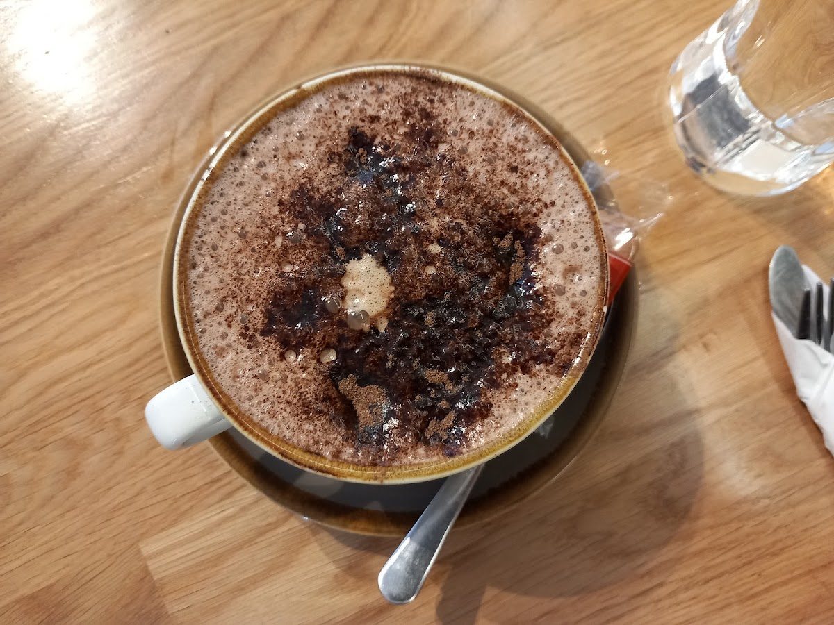 A hot chocolate topped with foam and grated chocolate on a saucer, on a wooden table.